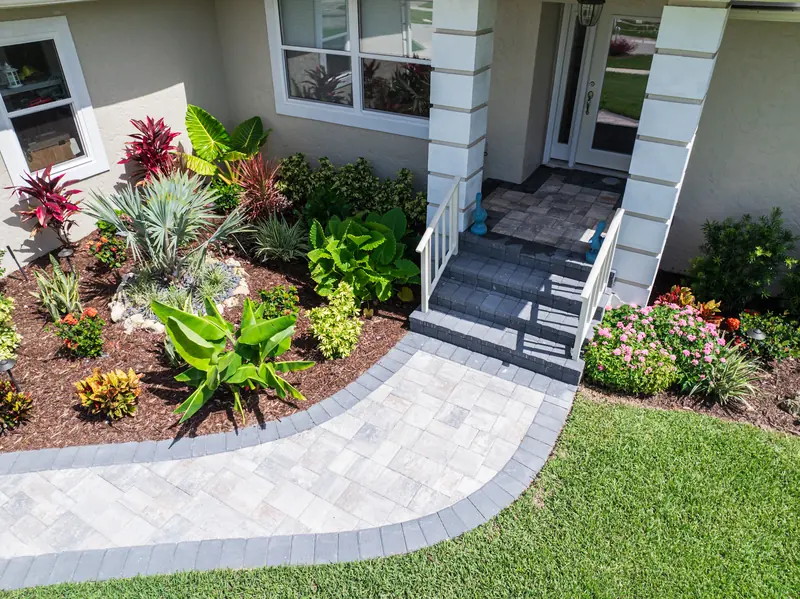Front entry bed with ti plants, bromeliads and flowering shrubs beside a paver walkway