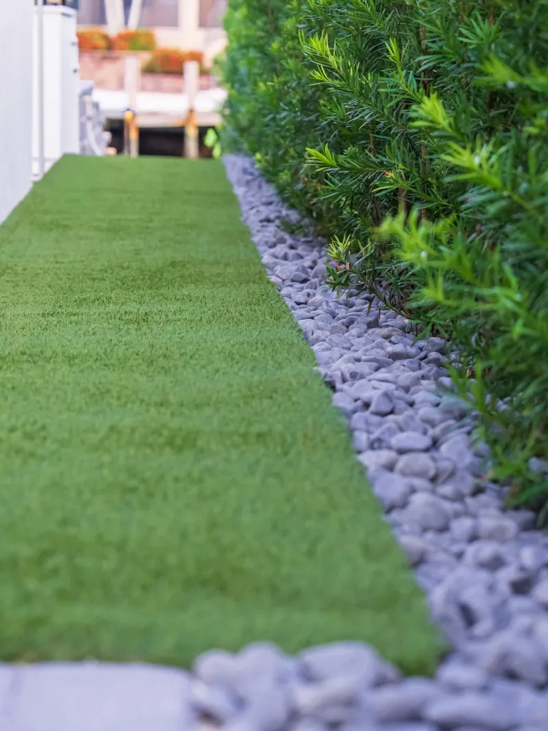 Artificial turf side yard edged with gray river rock beside a podocarpus hedge