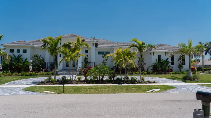Single-story white home framed by palms, tropical foliage and a planted circular driveway island